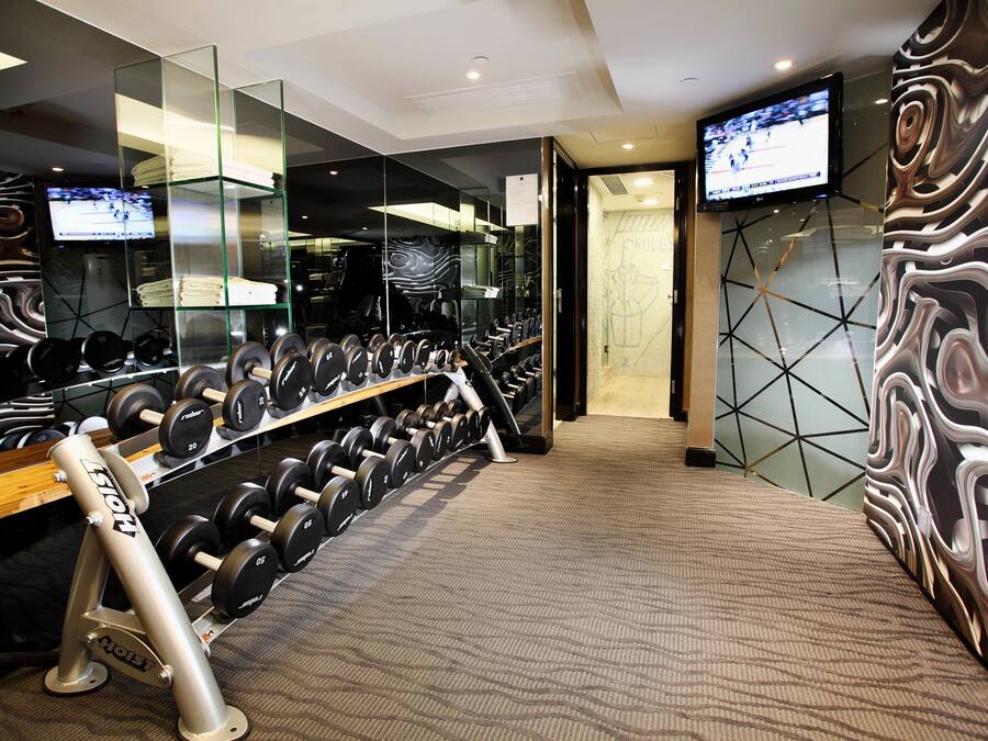 A gym with weightlifting equipment and a TV screen displaying a sports event.