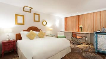 A hotel room with a large bed, a desk, a chair, and a dresser.