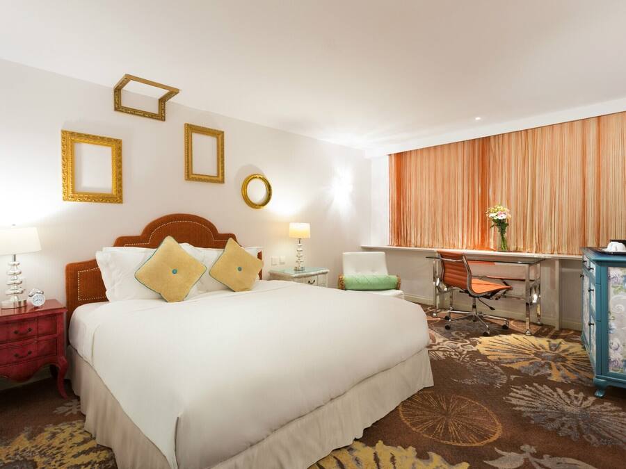 A hotel room with a large bed, a desk, a chair, and a dresser.