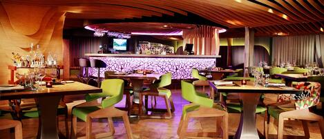 A modern restaurant with a bar area, wooden ceiling, and green chairs.