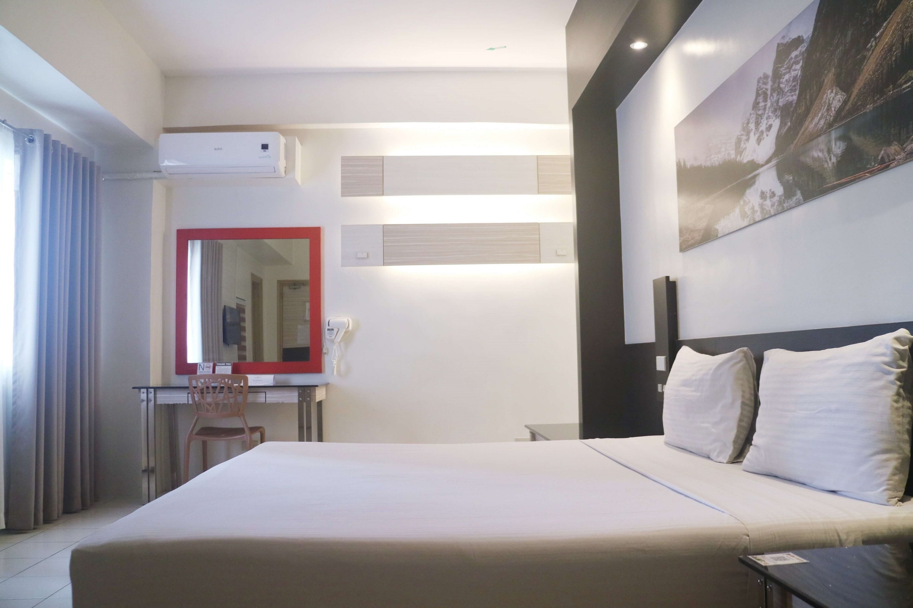 Hotelkamer met een bed, bureau, stoel, airconditioning, spiegel en een schilderij aan de muur.