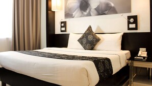 A hotel room with a bed, a nightstand, a telephone, and a wall-mounted picture.
