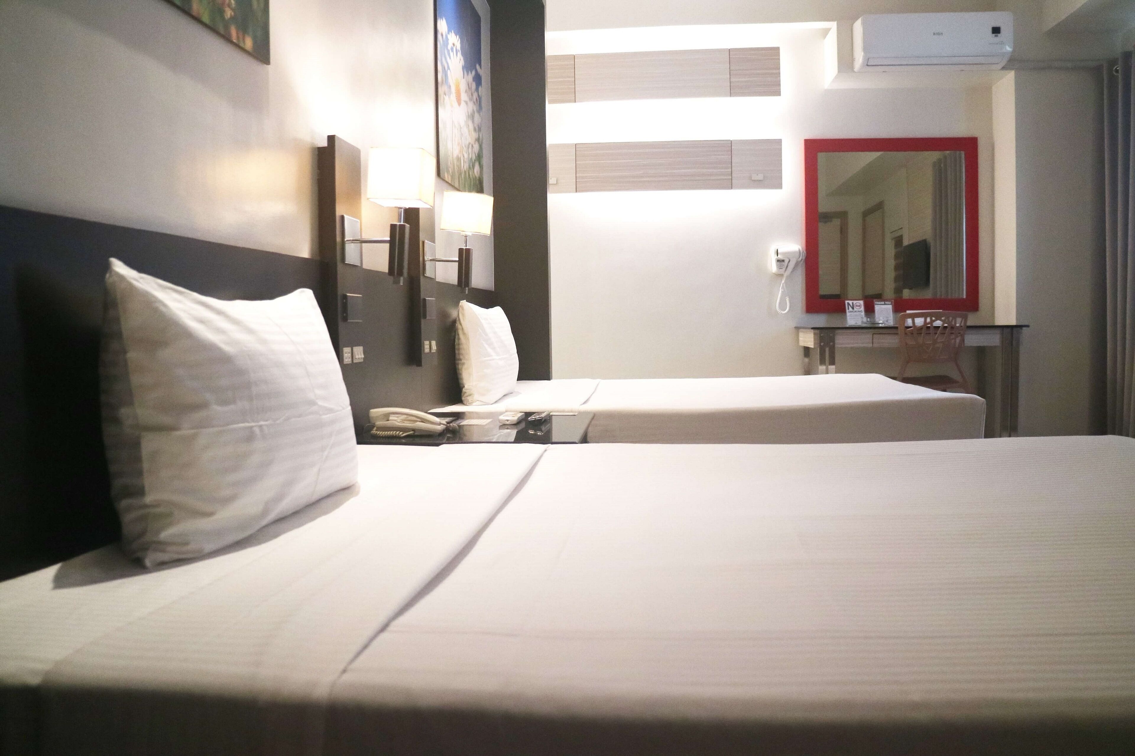 Ein Hotelzimmer mit zwei Betten, einem Schreibtisch mit Stuhl, einem Telefon und einem Spiegel.