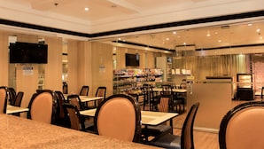 A restaurant with multiple tables and chairs, a television mounted on the wall, and a visible menu board.