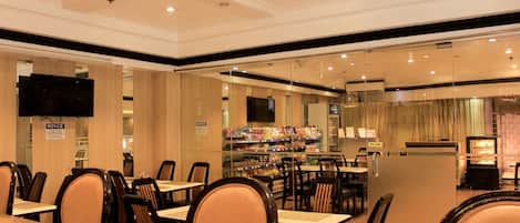 Un restaurante con varias mesas y sillas, un televisor montado en la pared y un menú a la vista.