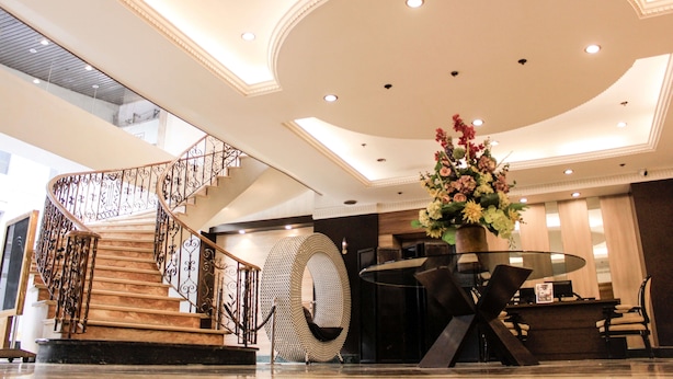 A hotel lobby with a marble staircase, a reception desk, and a large floral arrangement.