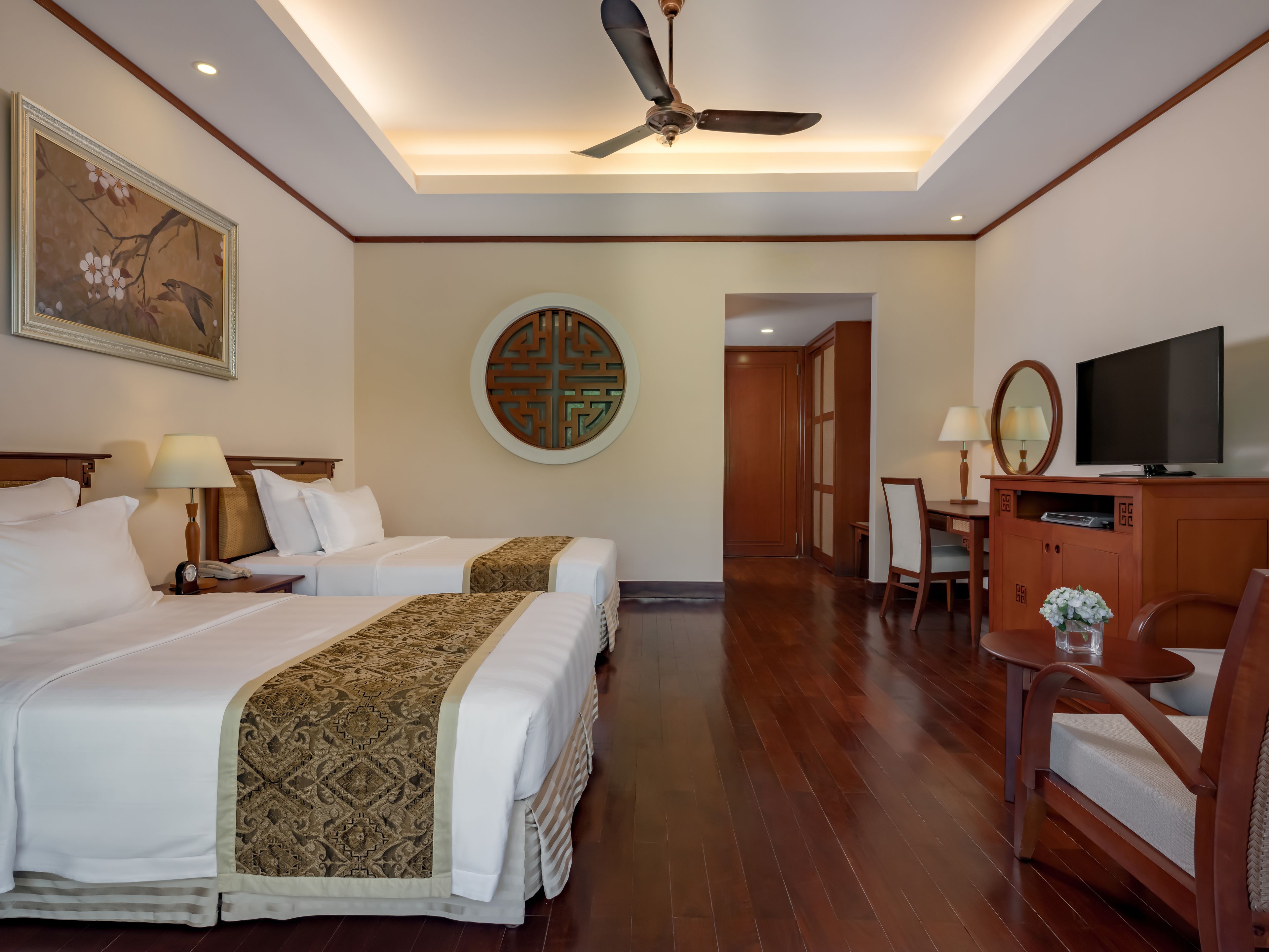 A hotel room with two beds, a ceiling fan, a TV, and a dining area.