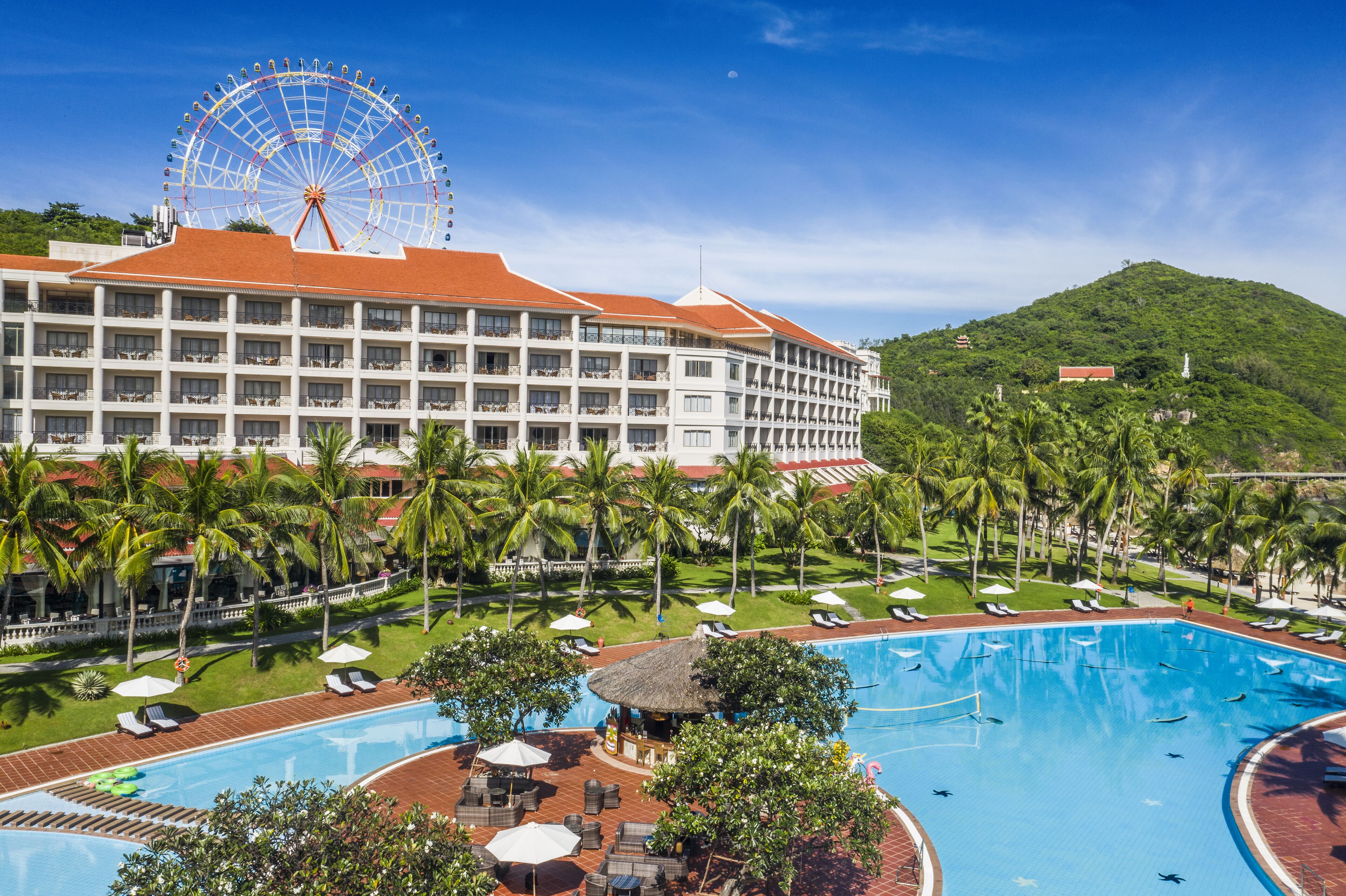 Un hôtel doté d’une grande piscine, de palmiers et, au loin, d’une grande roue.