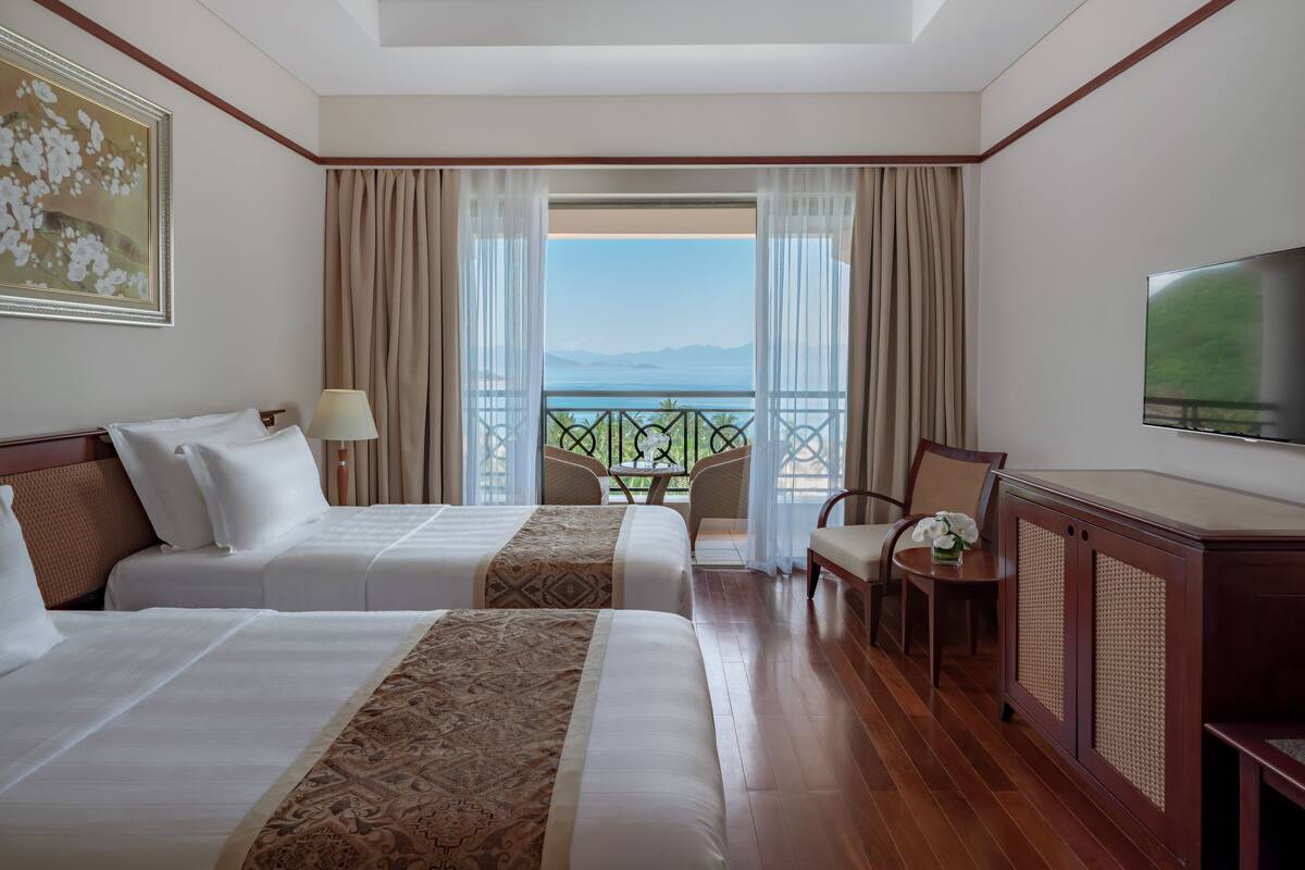 Hotelkamer met twee bedden, een televisie, een balkon met uitzicht op zee en een zithoek.