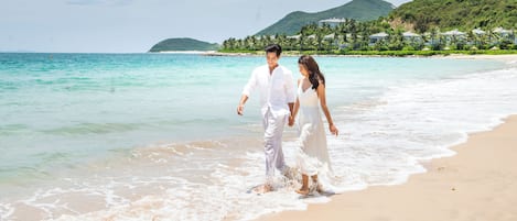 Um casal caminhando numa praia com águas turquesa cristalinas e montanhas ao fundo.