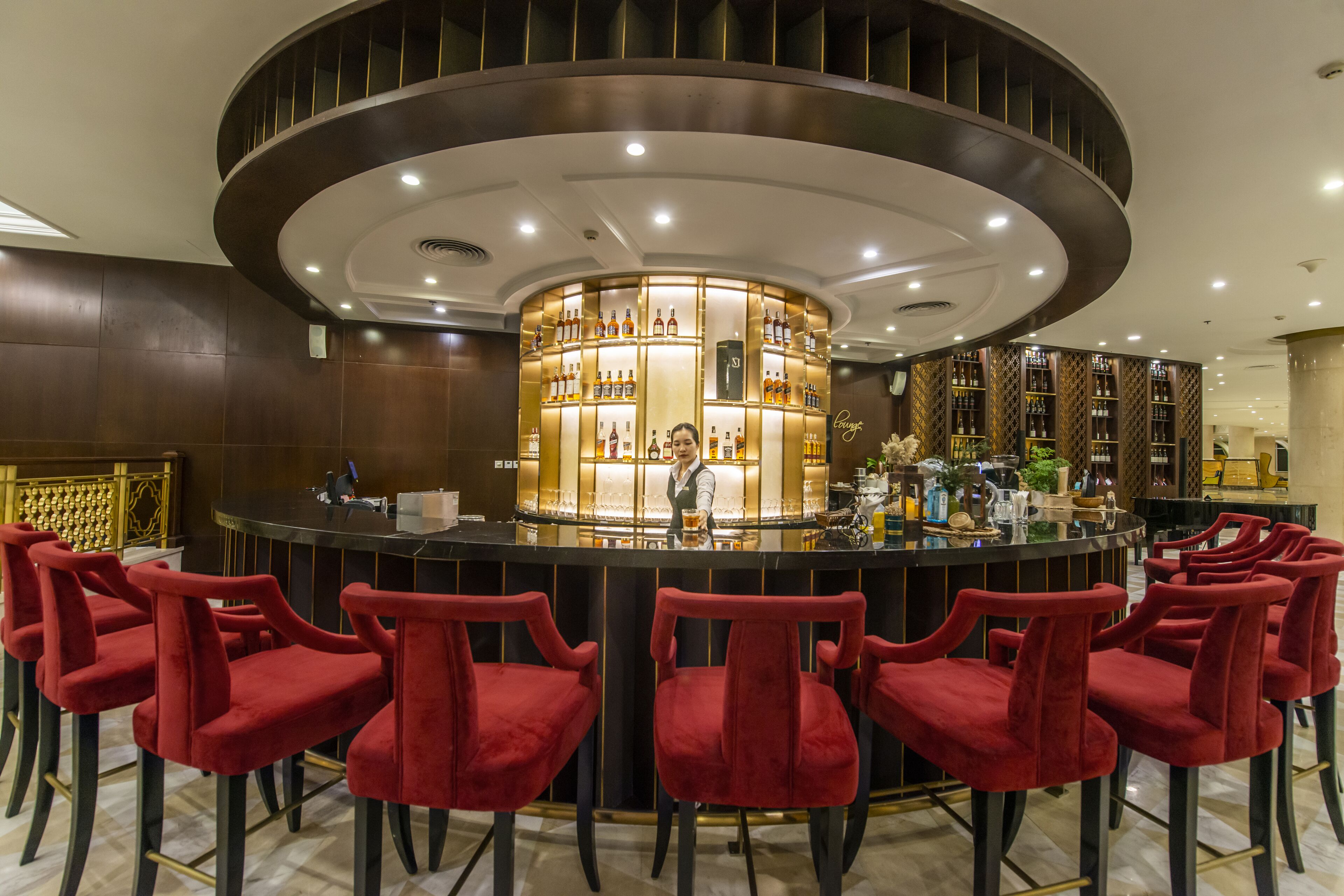 A bar area with a circular bar counter, red velvet chairs, and a bartender.