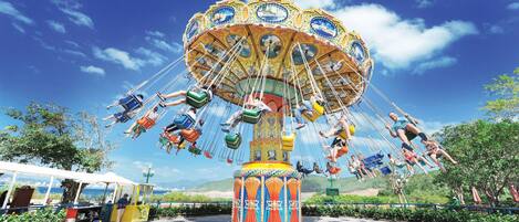Un carrousel doté de nombreuses places assises et d’une colonne centrale, entouré de verdure et sous un ciel dégagé.
