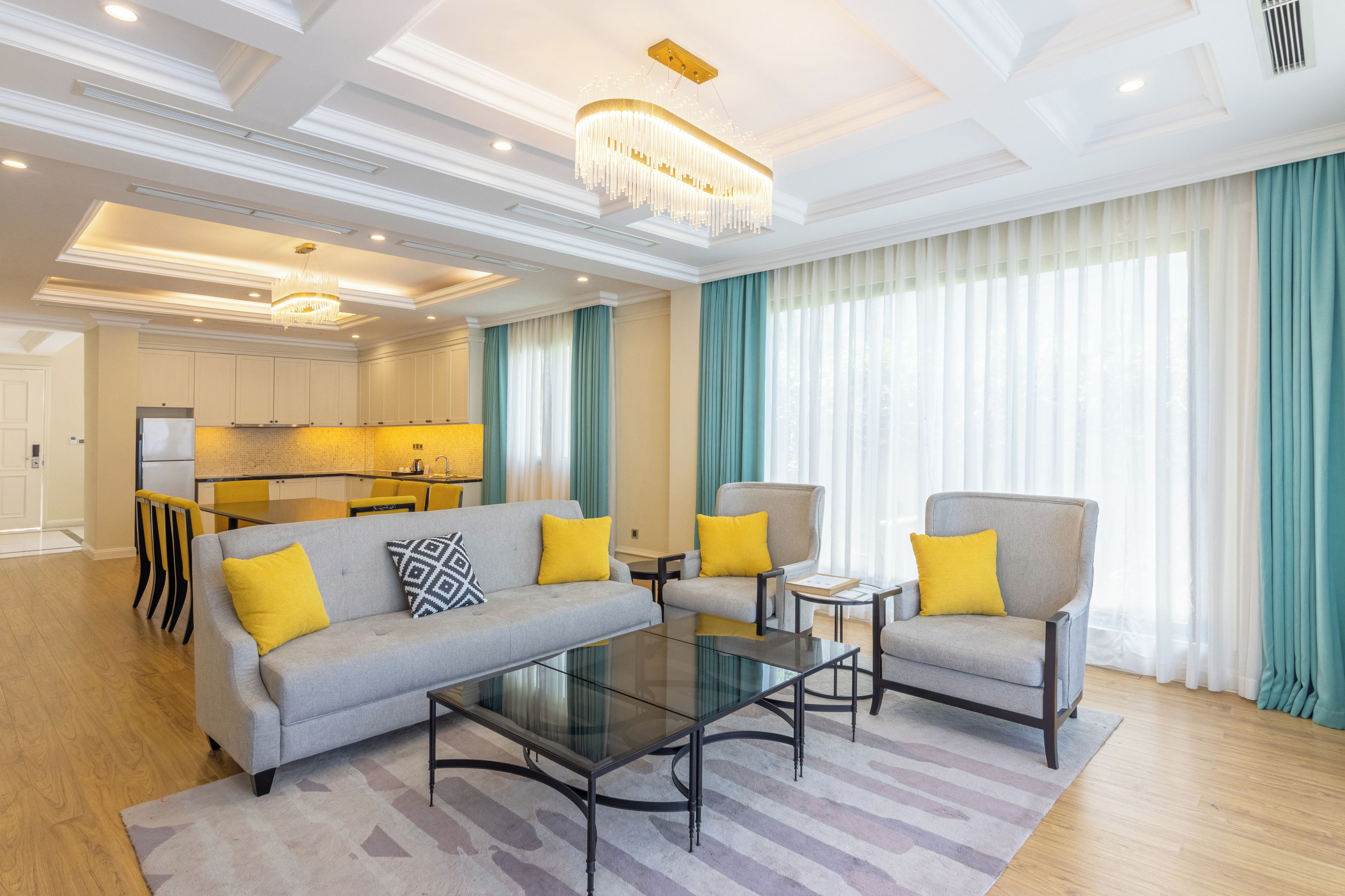 A modern living room with a sofa, armchairs, a glass coffee table, and a chandelier.