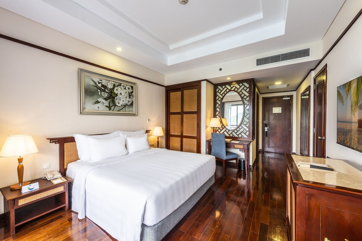 Een hotelkamer met een groot bed, nachtlampjes, een bureau met stoel en een schilderij aan de muur.