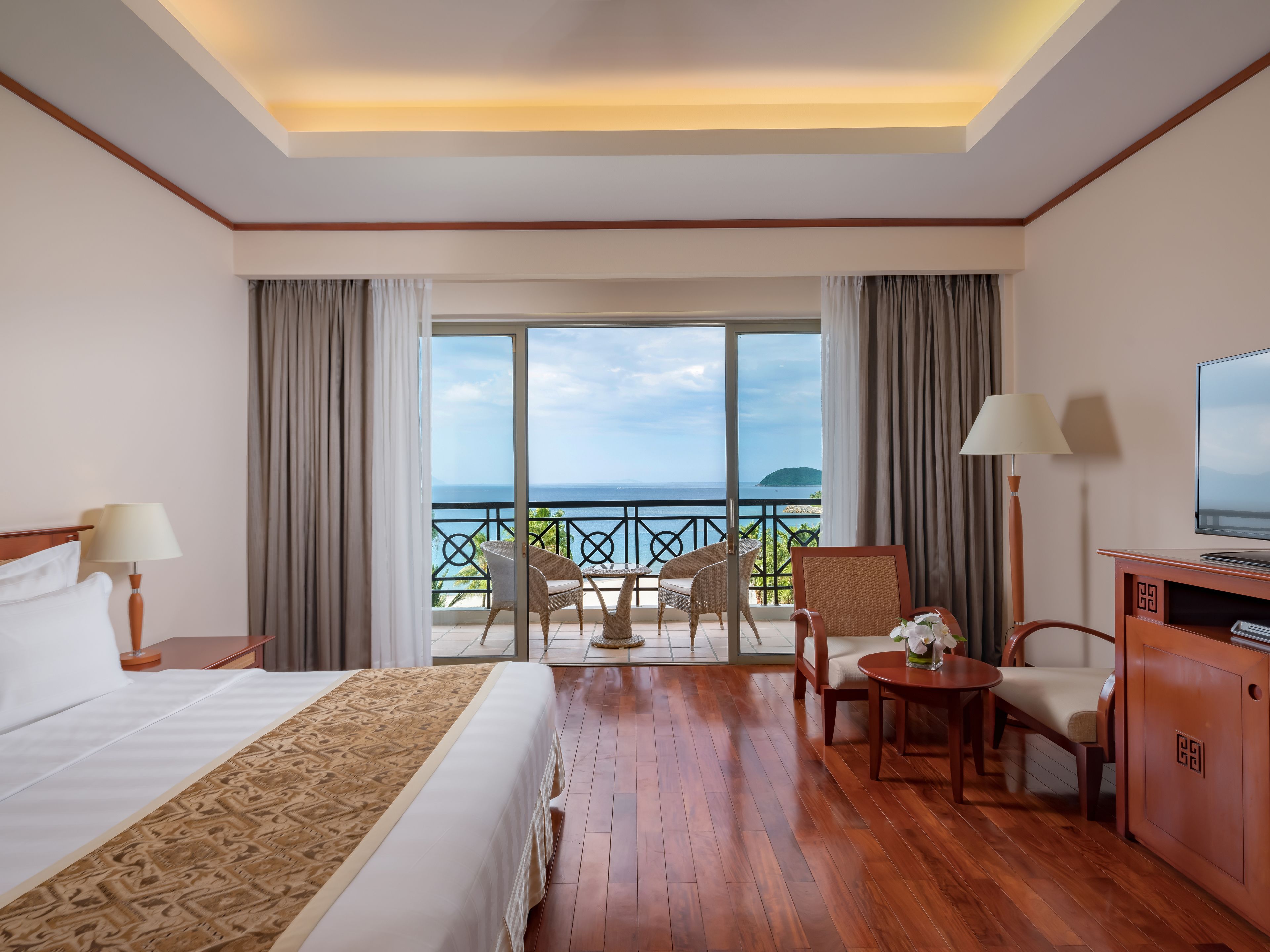 Ein Hotelzimmer mit Bett, Schreibtisch, Stuhl, Fernseher und einem Balkon mit Meerblick.