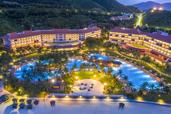A resort with a large central pool, multiple guest buildings, and surrounding palm trees.