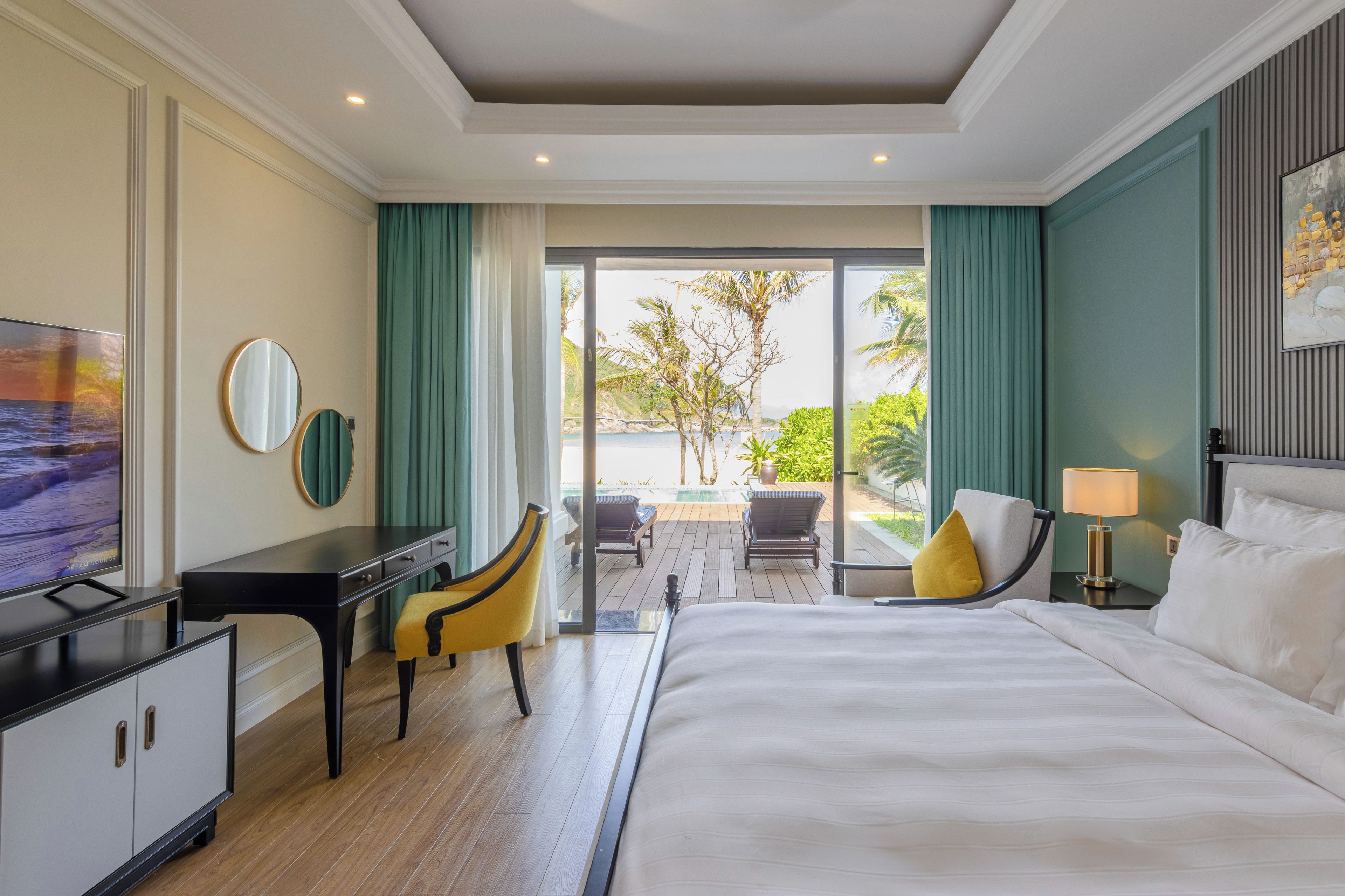 Habitación de hotel con una cama, un escritorio con televisor, una silla, una lámpara y vistas al exterior.