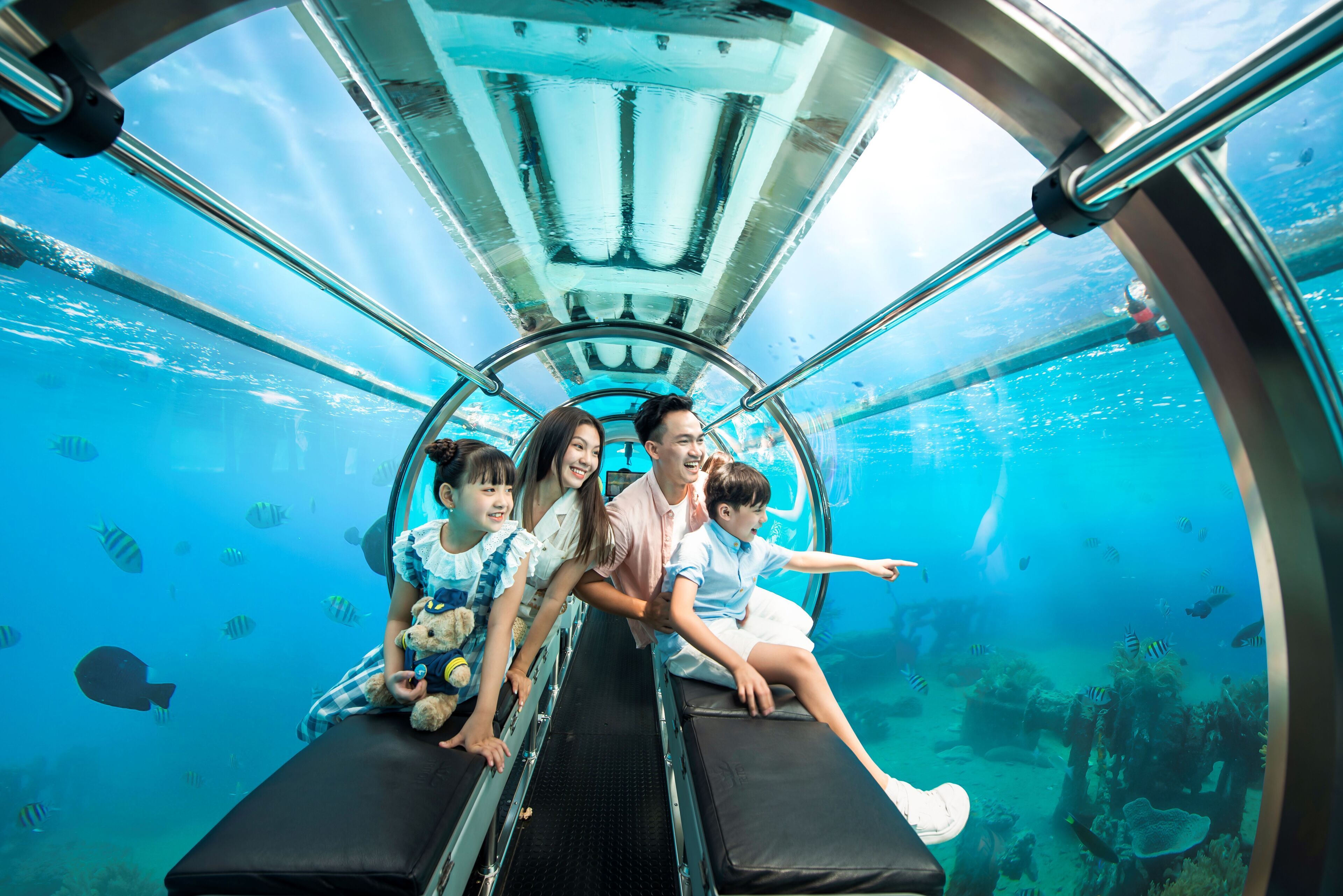 Una familia dentro de un túnel submarino con agua cristalina y vida marina visible.