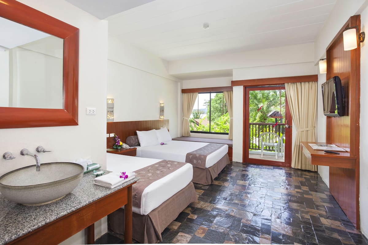 A hotel room with a large mirror, a sink, two beds, a small table, and a TV.