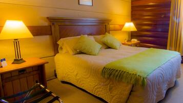 Habitación de hotel con una cama grande, dos lámparas de noche, un cabecero de madera, una mesita con lámpara y una silla.