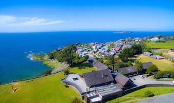 Vista aérea de un pueblo costero con casas, una carretera y un edificio grande con techo curvo.