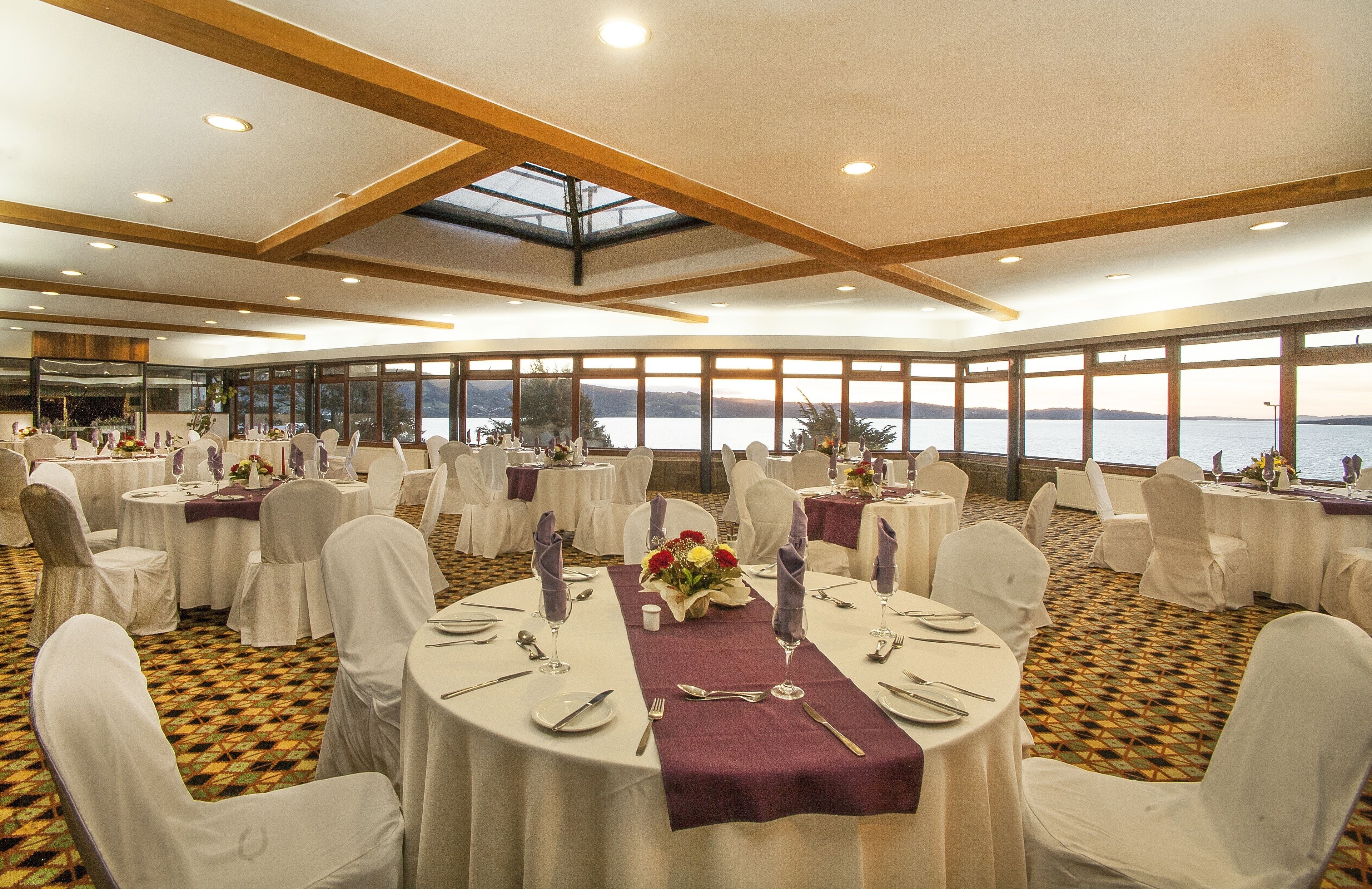 A banquet hall with round tables, white chairs, and a view of the water.