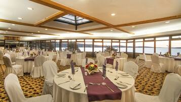 A banquet hall with round tables, white chairs, and a view of the water.