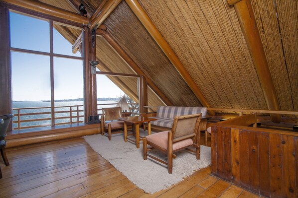 A wooden interior with a high ceiling, a large window overlooking a body of water, and a seating area with a sofa and chairs. - Hotel Panamericana Ancud (Ancud)