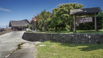 Une enseigne indiquant l’emplacement de l’Hostería Ancud, un hôtel dont l’entrée est marquée par un mur de pierre et dont le bâtiment principal est en bois, visible à l’arrière-plan.