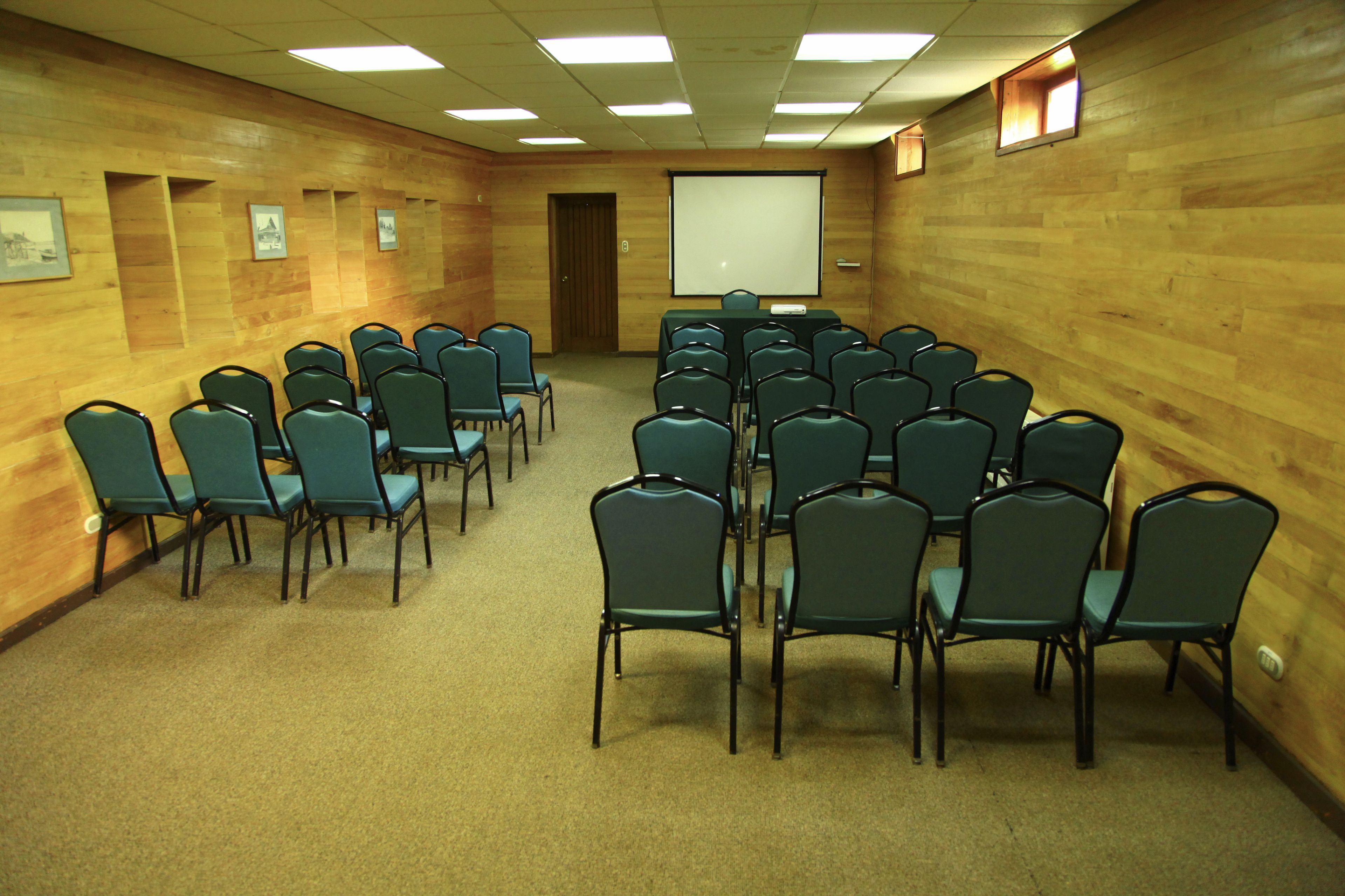A conference room with rows of chairs, a projector screen, and framed pictures on the walls.