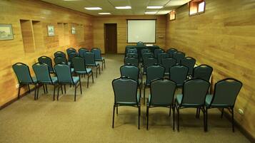 A conference room with rows of chairs, a projector screen, and framed pictures on the walls.