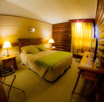 Una habitación de hotel con una cama grande, dos lámparas de noche, un cabecero de madera, un escritorio con una silla y una ventana con cortinas.