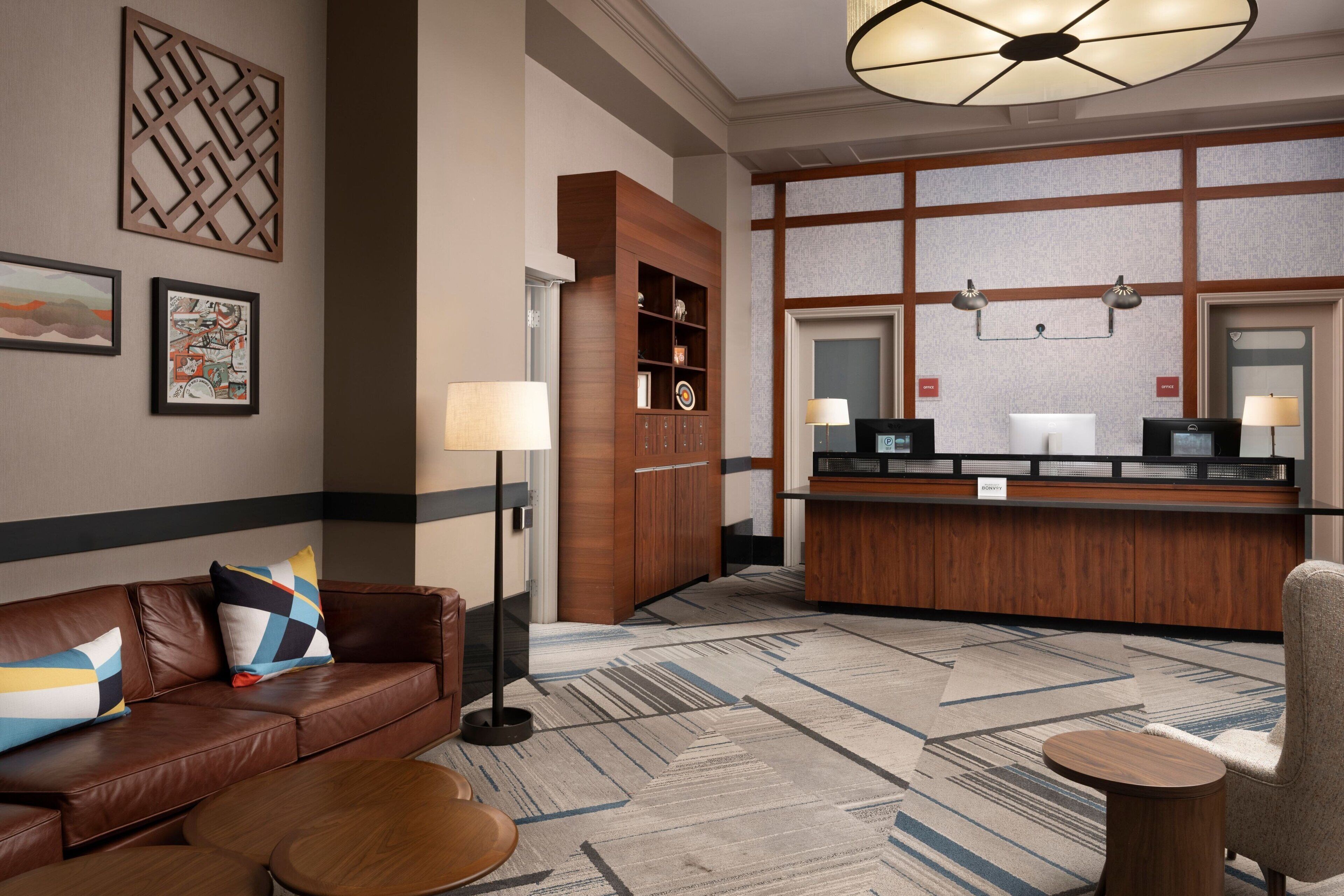 A hotel lobby with a reception desk, a brown leather sofa, a coffee table, and a patterned carpet.