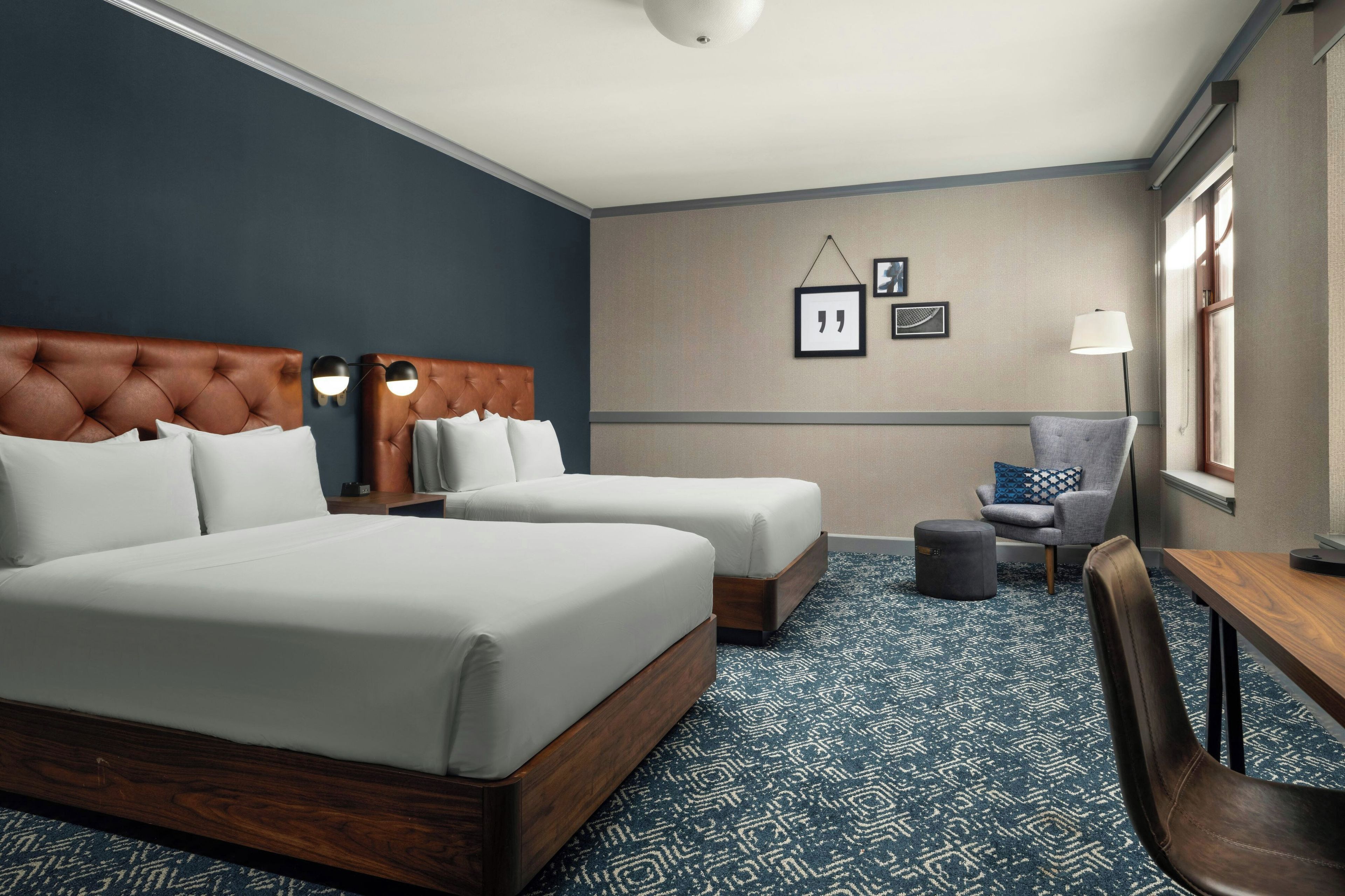 A hotel room with two beds, a desk, a chair, and a small table.
