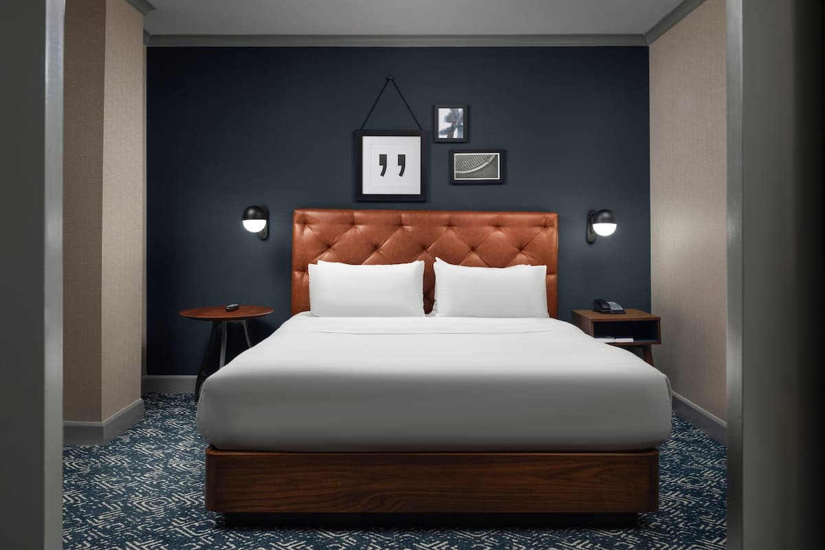 Une chambre d’hôtel avec un grand lit, une tête de lit en bois, deux tables de chevet et une petite table ronde.