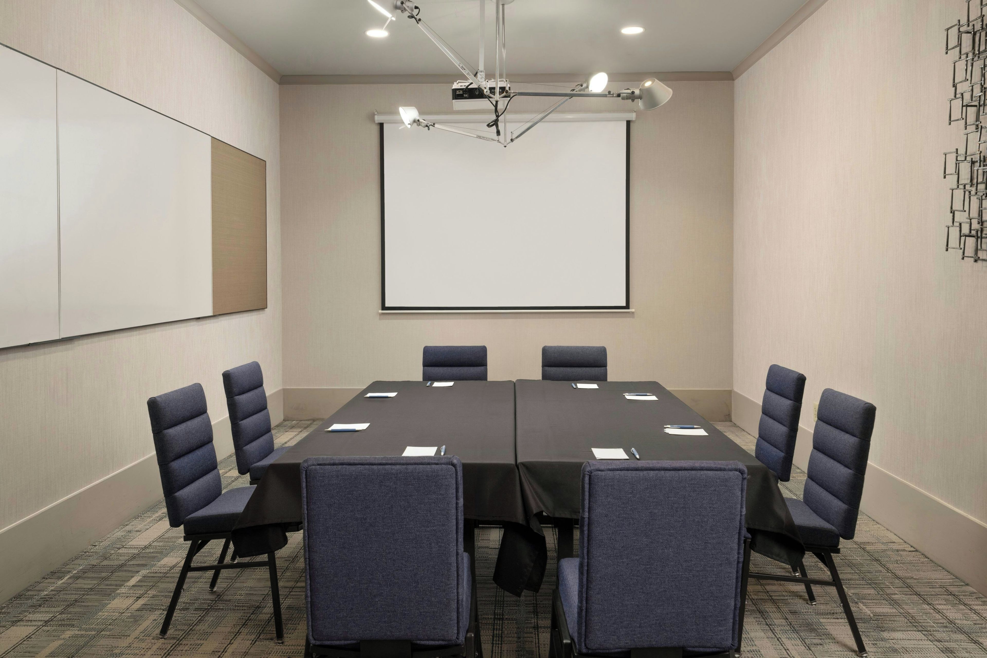 A conference room with a large table, six chairs, a projector screen, and a whiteboard.
