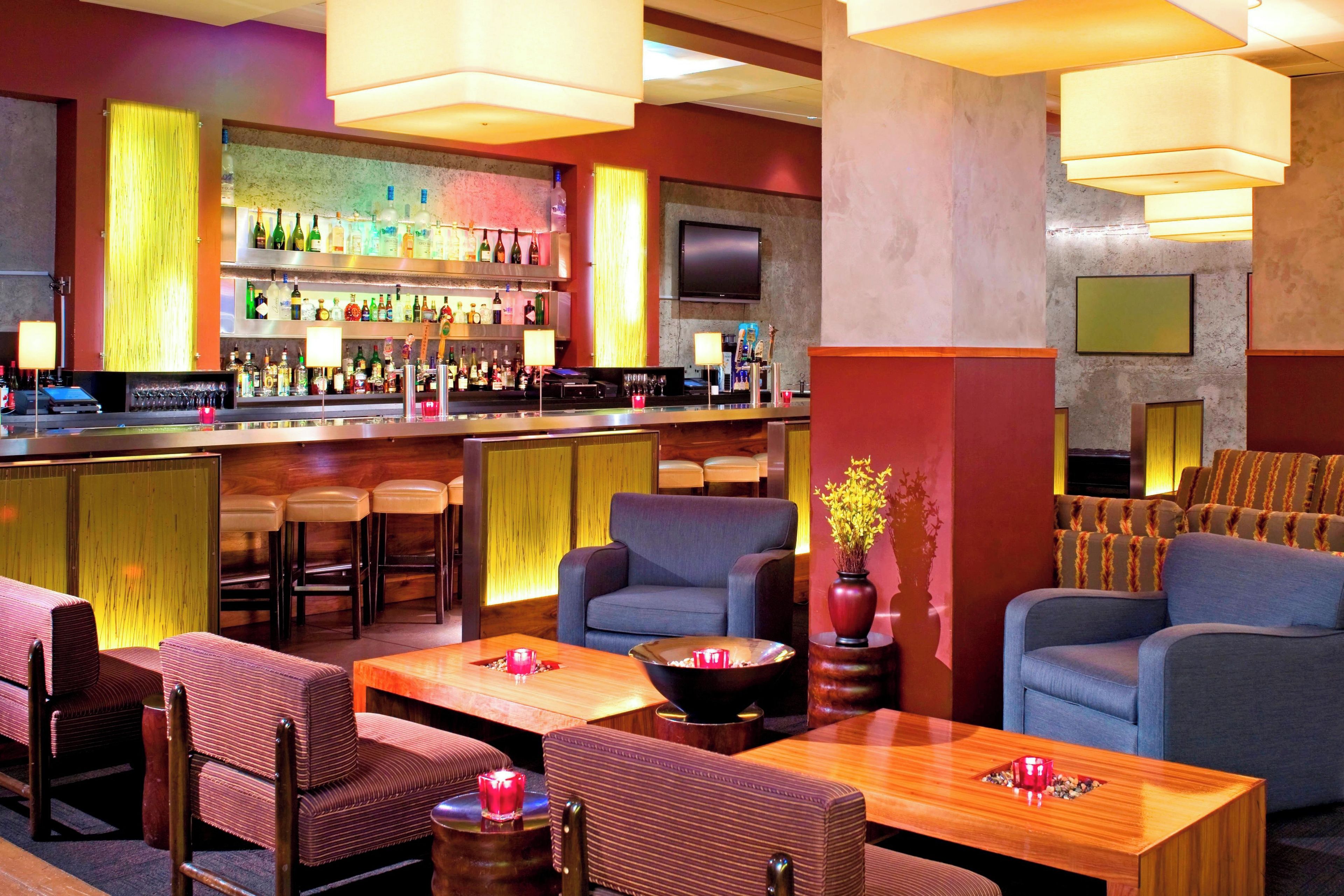 A bar area with multiple seating options, a television mounted on the wall, and a variety of bottles on the shelves.