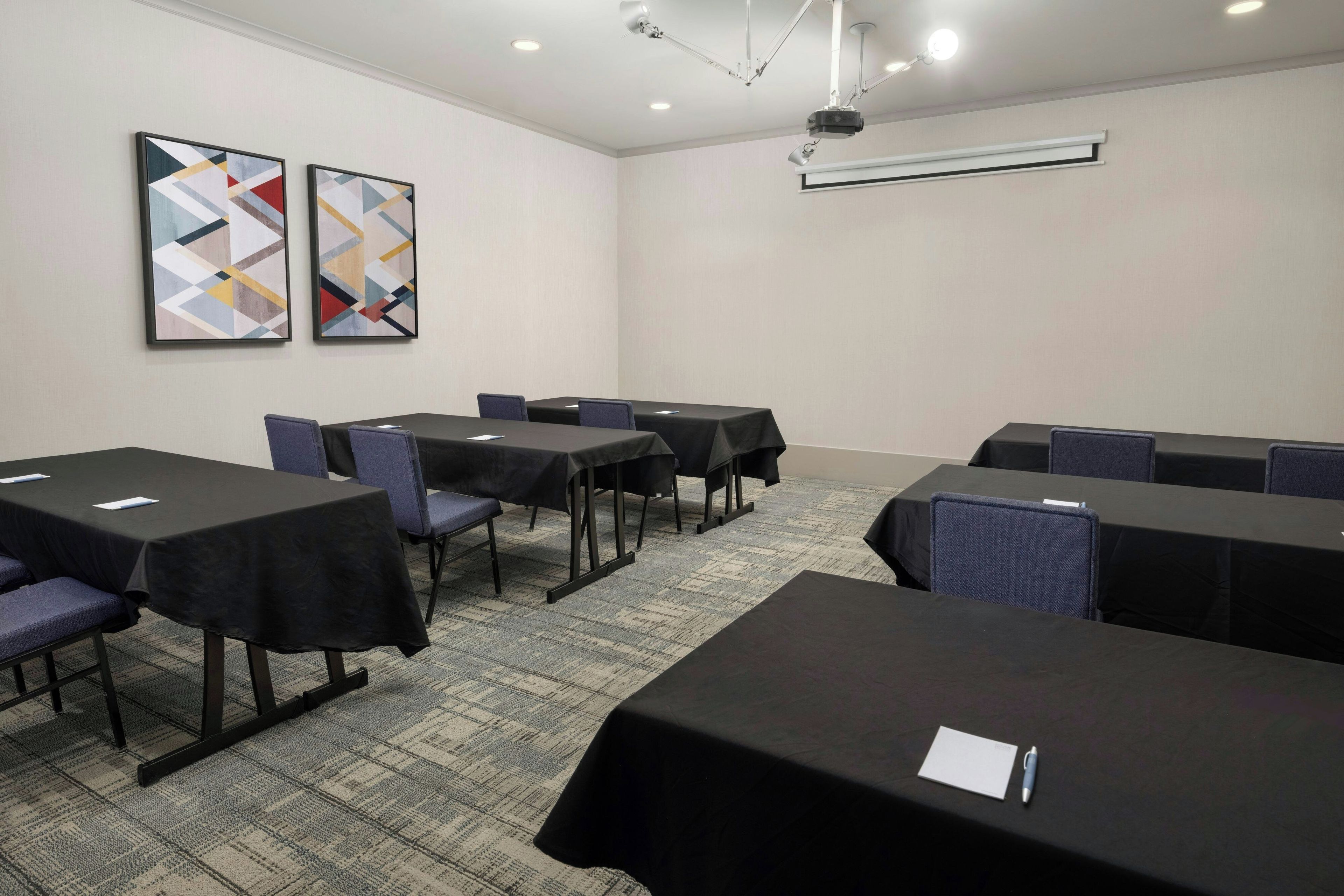 Une salle de conférence équipée de tables, de chaises et d’un projecteur.