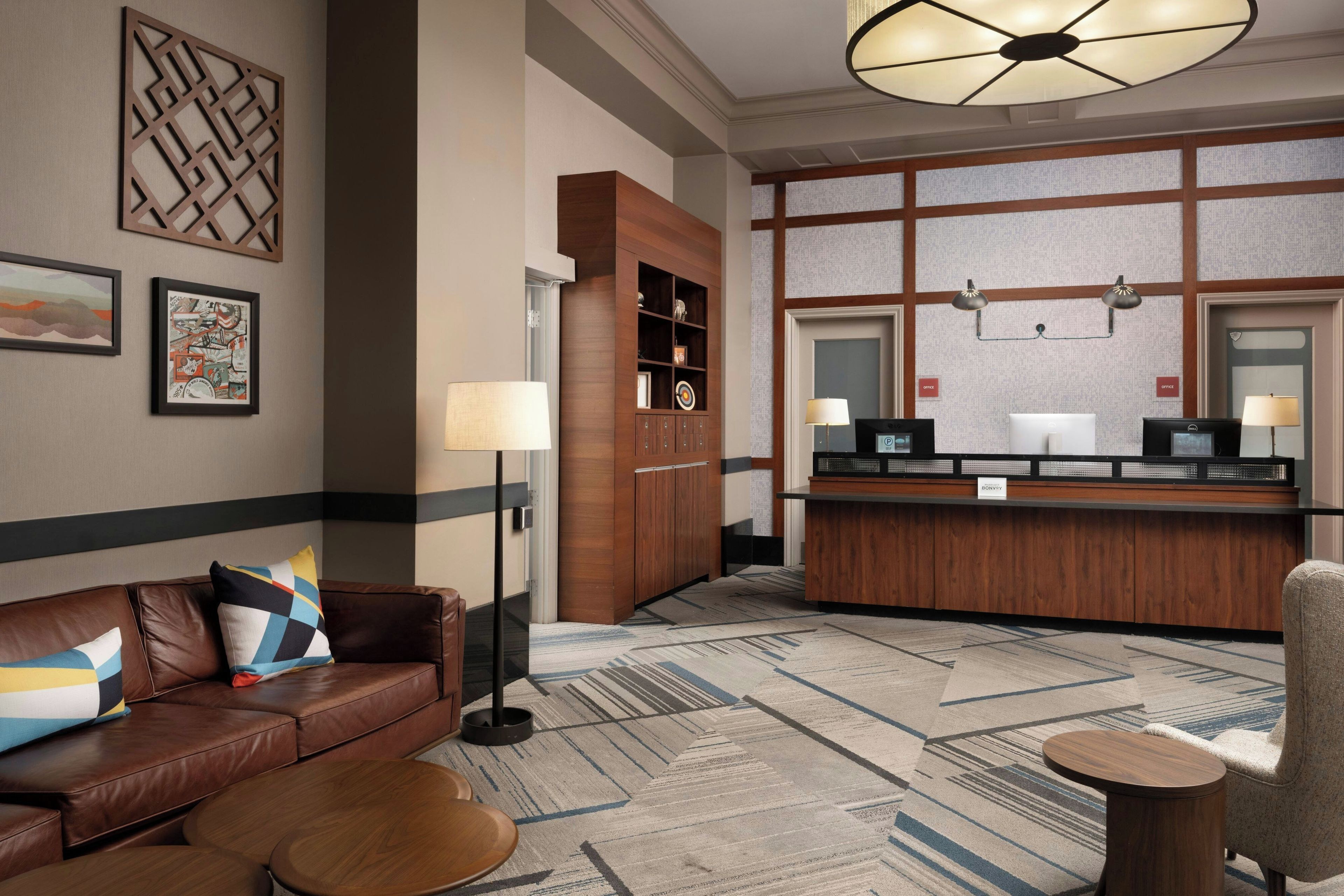 A hotel lobby with a reception desk, a brown leather sofa, a patterned carpet, and framed artwork on the walls.