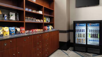 A kitchenette with a refrigerator stocked with beverages and a shelf with snacks.