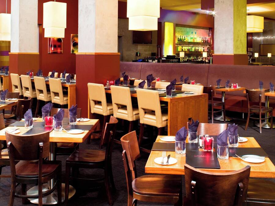 Restaurante com várias mesas e cadeiras, área de bar ao fundo e um espaço de estar com bancos acolchoados.