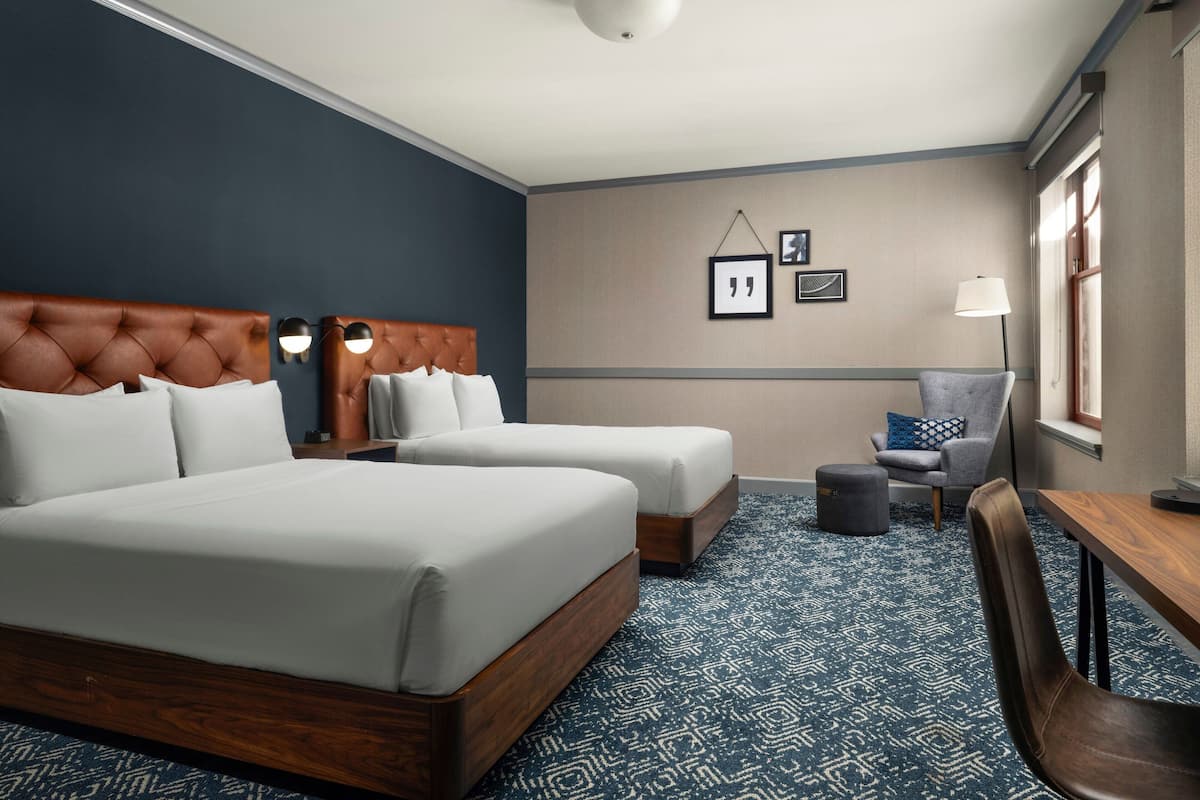 Une chambre d’hôtel avec deux lits, un bureau, une chaise et une petite table.