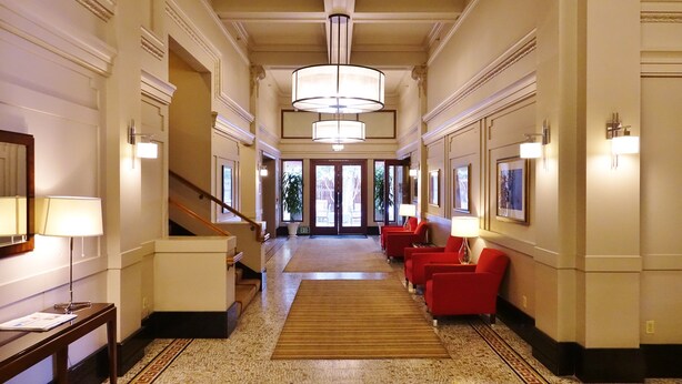 Een ruime hotellobby met een weelderige kroonluchter, een trap en rode zitplaatsen langs de muren.