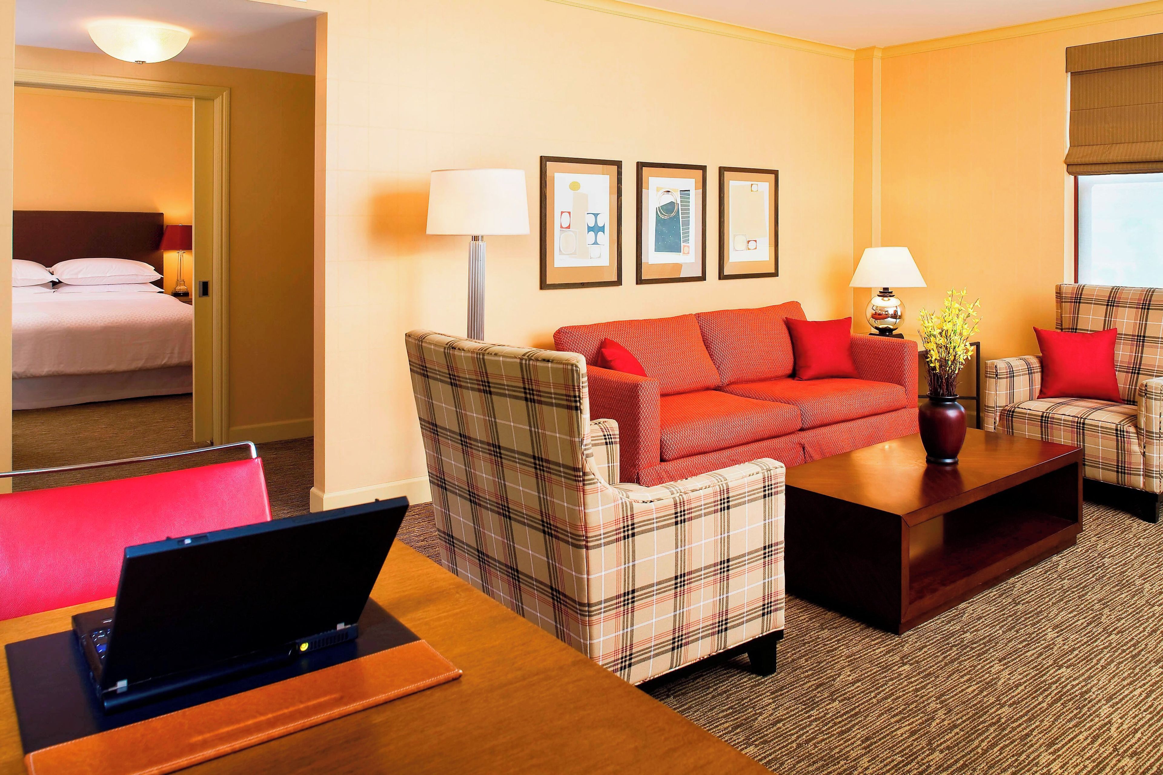 Ein Hotelzimmer mit einem Bett, einem Schlafsofa, einem Sessel, einem Couchtisch und einem Schreibtisch mit einem Laptop.