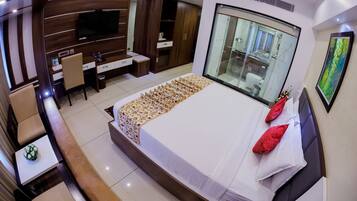 A modern hotel room with a large bed, a desk, a TV, and a bathroom visible through a glass partition.