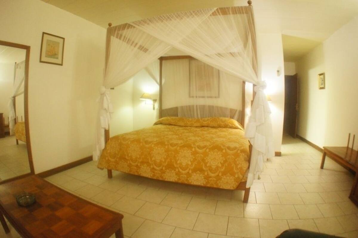 A bedroom with a four-poster bed, a wooden nightstand, a mirror, and a bedside table.