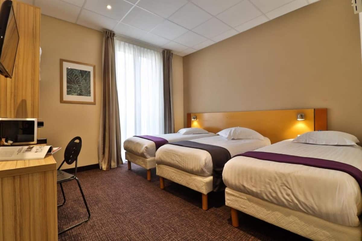 A hotel room with two beds, a desk, a chair, and a TV.