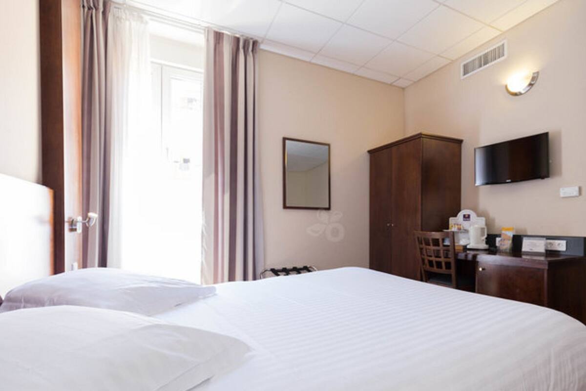 A hotel room with a large bed, a desk with a chair, a television, and a wardrobe.