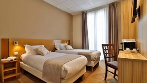 A hotel room with two beds, a desk, a chair, a TV, and a window with curtains. - Hotel le Noailles Nice Gare (Nice)