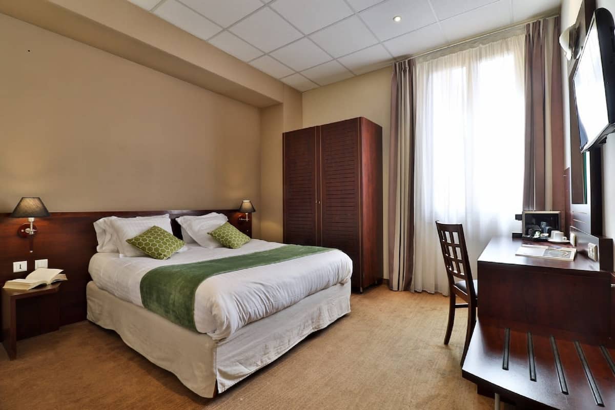 A hotel room with a bed, a desk, a wardrobe, and a television.